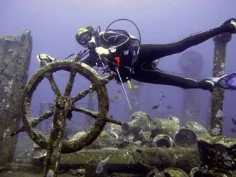 A diver at a wreck's ship wheel in a stiff current